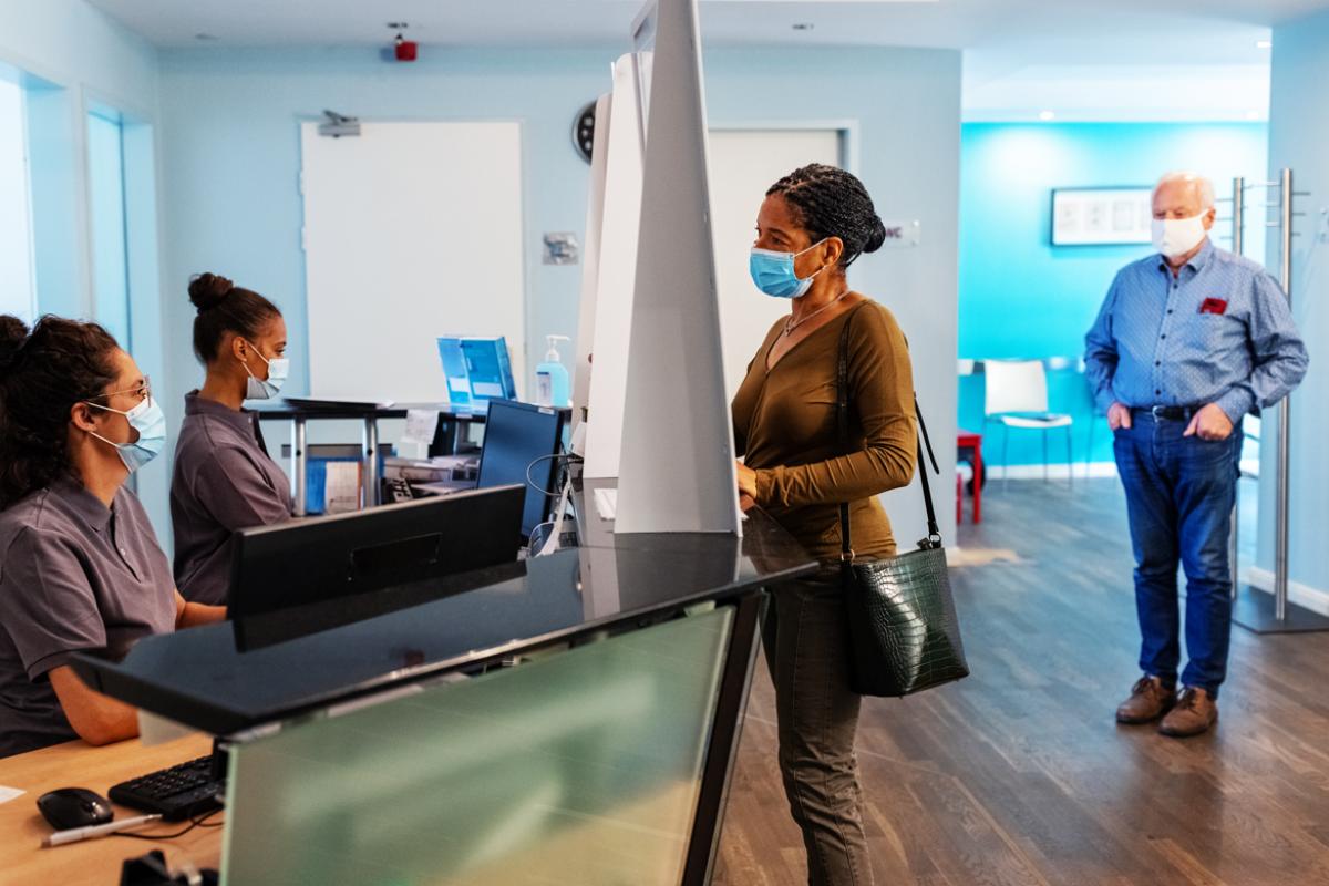 Patient checking in at a physician's office with patients and office staff wearing masks