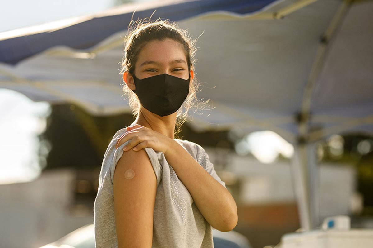 Smiling person holding up a sleeve to show a bandaged arm from a vaccine