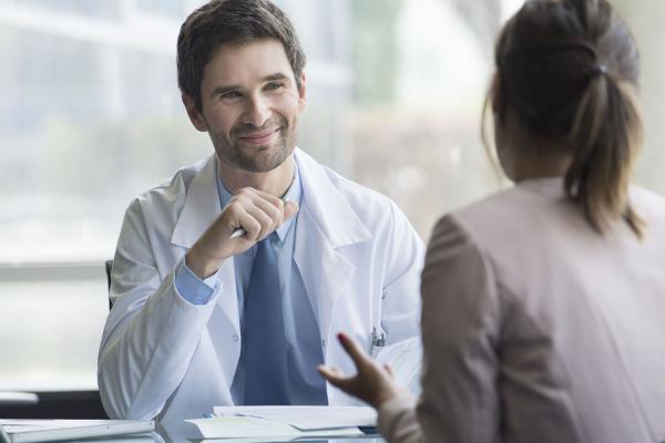 A smiling resident sits at a desk and listens to a colleague.